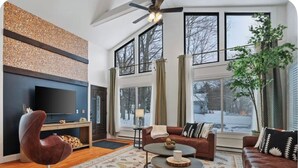 Ein modernes Wohnzimmer mit Kamin, großen Fenstern und Deckenventilator.