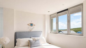 Een slaapkamer met een bed, een aan de muur bevestigde droomvanger en een raam met uitzicht op zee.