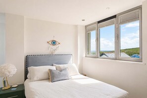 Un dormitorio con cama, un atrapasueños colgado en la pared y ventana con vista al mar.