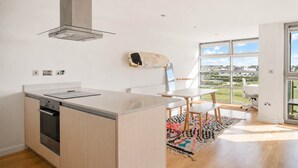 Een moderne keuken met een groot eiland, een ingebouwde oven en uitzicht op een groen landschap door grote ramen.