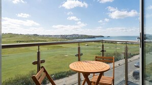 Een balkon met een tafel en stoelen, met uitzicht op een kustlandschap met een golfbaan en een weg.