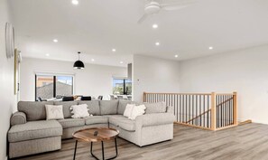 Ein modernes Wohnzimmer mit einem Ecksofa, einem runden Couchtisch und einer Treppe mit Holzbalkon.