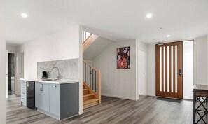 Eine moderne Küche mit eingebautem Geschirrspüler, einer Holztreppe und einer Tür mit vertikalen Lamellen.