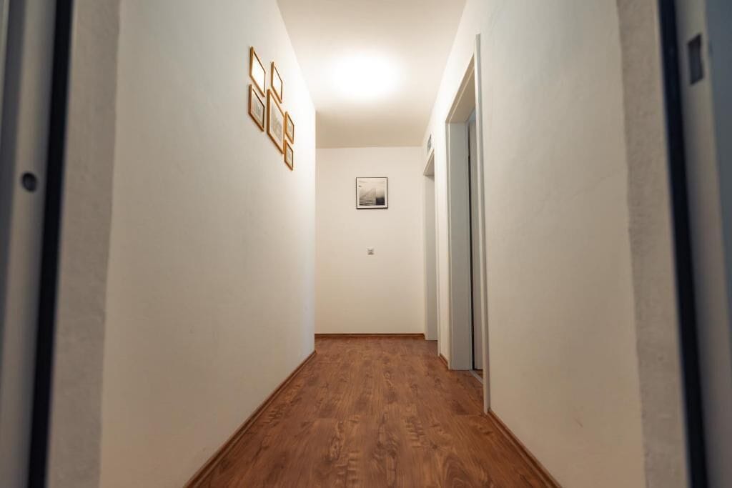 A narrow hallway with wooden flooring, white walls, and a framed picture on the wall.