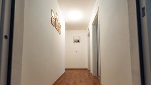 A narrow hallway with wooden flooring, white walls, and a framed picture on the wall. - Hotel Three Corners (Grenzach-Wyhlen)