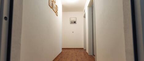 A narrow hallway with wooden flooring, white walls, and a framed picture on the wall.