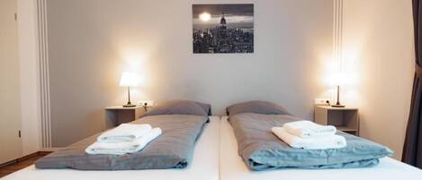 A hotel room with two beds, each with a pillow, a nightstand with a lamp, and a framed picture on the wall.