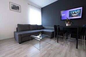 A modern living room with a grey sofa, a glass coffee table, and a TV mounted on the wall displaying a Batman game.