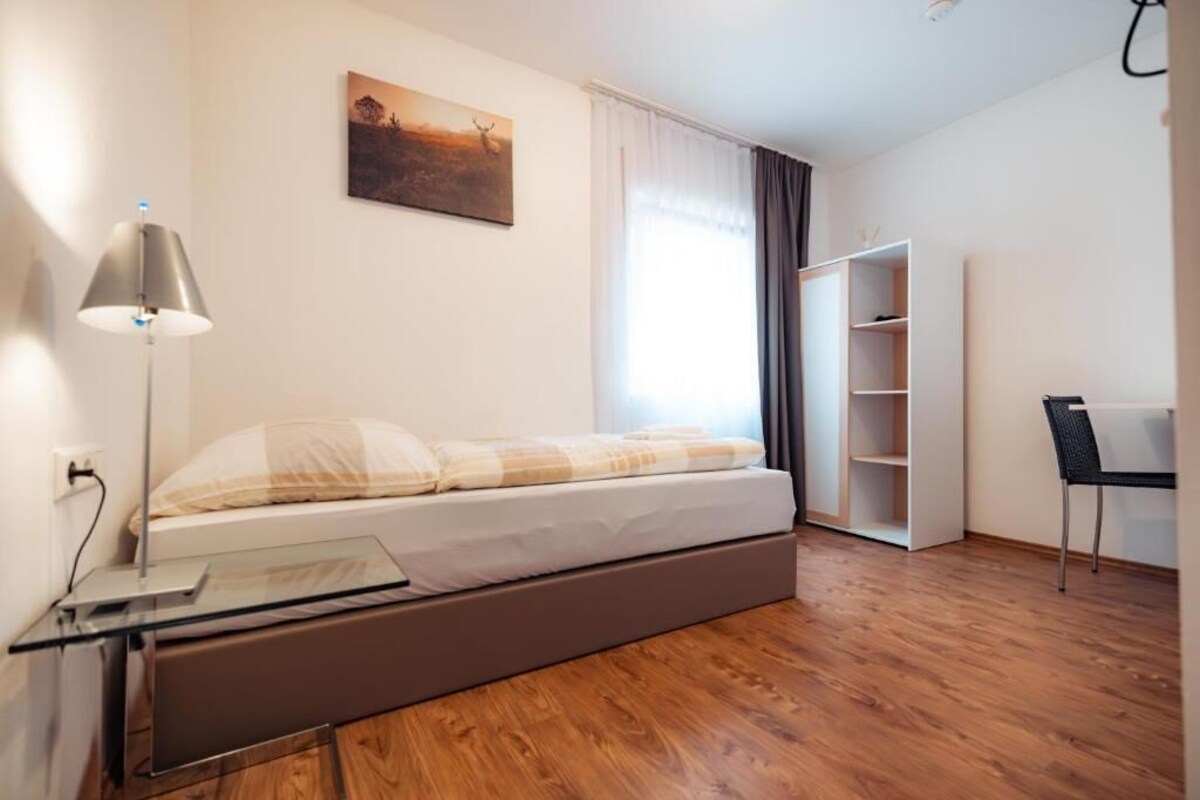 A modern bedroom with a bed, bedside table, lamp, and a painting on the wall.