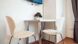 A room with a white table and two chairs, a small potted plant, and a TV mounted on the wall. - Hotel Three Corners (Grenzach-Wyhlen)