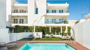 En modern byggnad i två våningar med en swimmingpool, utomhusmöbler och en välskött trädgård.