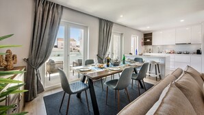 Ett modernt kök med vita skåp, en matplats med ett bord för fyra personer och en utsikt över staden genom stora fönster.