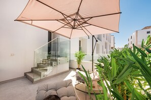 A balcony with a glass railing, a beige sofa, a large umbrella, and potted plants. - Elegant Apartment with Pool View (Tavira)