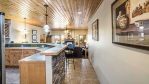 Une cuisine avec un plafond en bois, un plan de travail en pierre et un coin bar avec des tabourets.