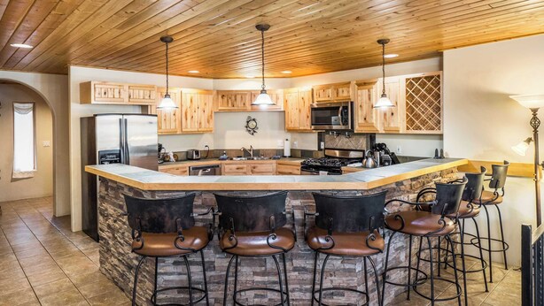 Une cuisine avec des meubles de rangement en bois, un îlot central doté de tabourets de bar et un mur d’accent en pierre.