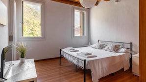 A bedroom with a bed, bedside tables, a desk, a potted plant, and two windows with a view of greenery. - Rabi Rooms (Valbrenta)