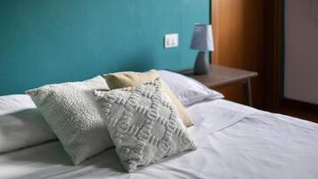A bed with white bedding and two textured pillows, a bedside table with a lamp, and a teal wall.