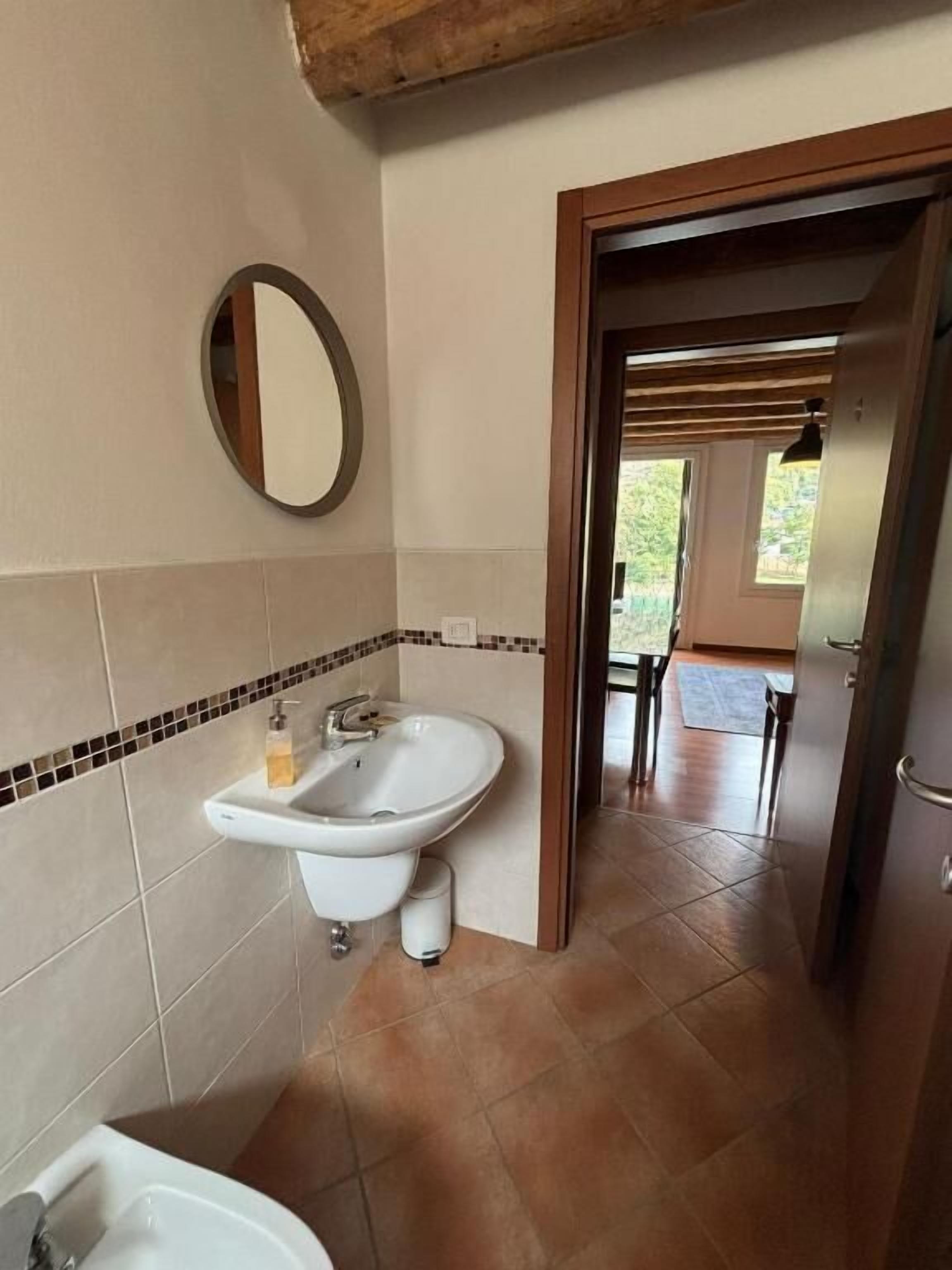 Un baño con lavamanos, espejo y suelo de baldosas.