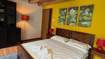 A bedroom with a wooden ceiling, a bed with white linens, a blue rug, and two paintings on the wall.