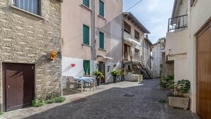 A narrow cobblestone street with buildings on either side, a table with chairs outside one building, and potted plants. - Rabi Rooms (Valbrenta)