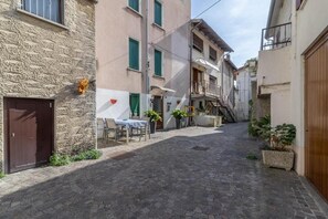 A narrow cobblestone street with buildings on either side, a table with chairs outside one building, and potted plants. - Rabi Rooms (Valbrenta)