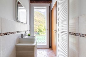 Un baño con lavamanos, espejo y vista a un balcón con montañas al fondo.