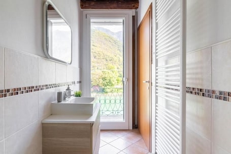 A bathroom with a sink, mirror, and a view of a balcony with a mountain backdrop.. Rabi Rooms