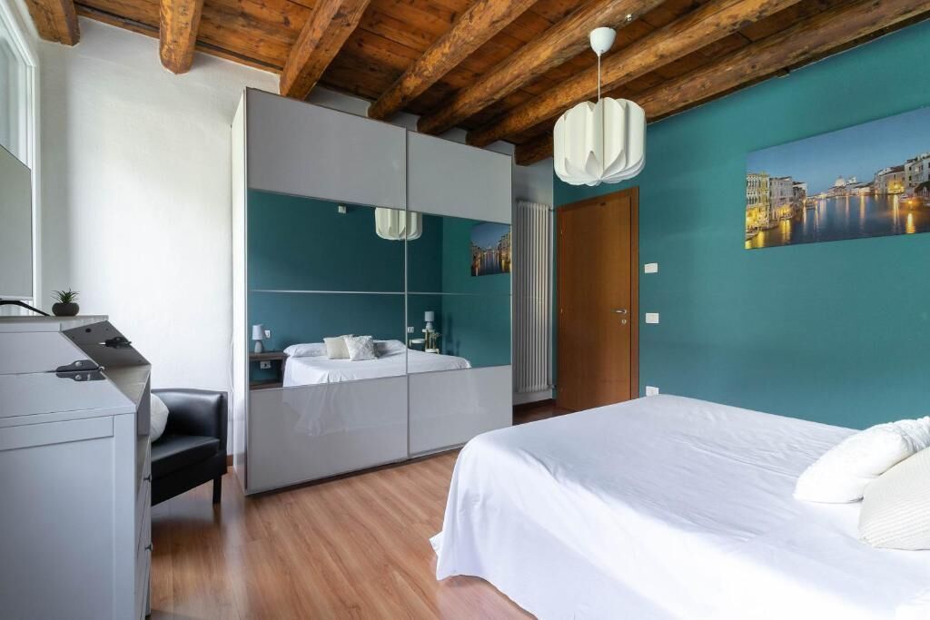 A bedroom with a bed, a desk, a mirror, a wardrobe, and a painting on the wall.