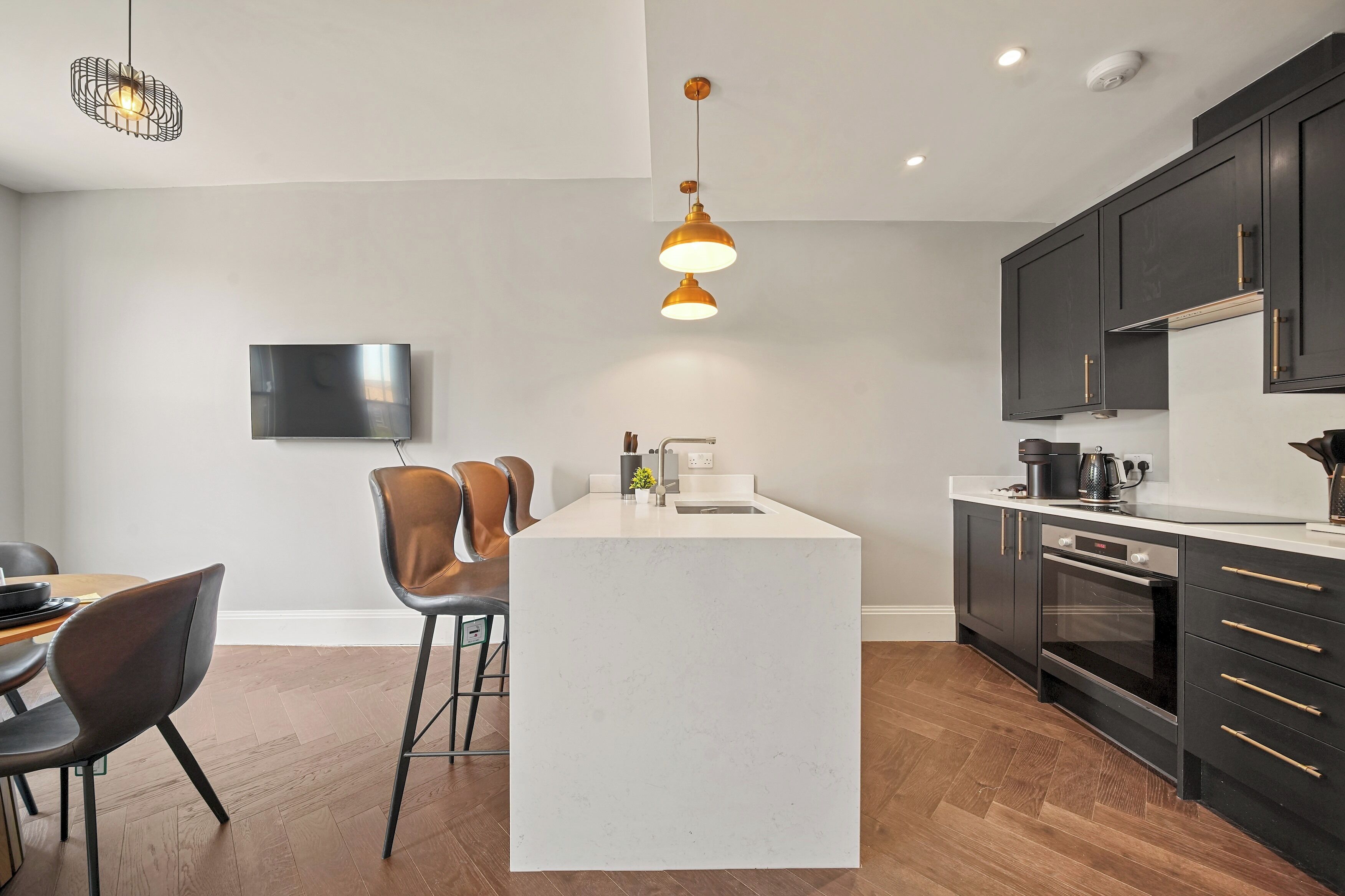 Une cuisine moderne dotée d’un îlot central, de meubles de rangement aux couleurs sombres et d’un téléviseur à écran plat fixé au mur.