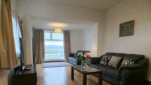 A living room with a sofa, a coffee table, a TV, and a large window with curtains. - Large coastal home in the countryside of Amlwch - Pass the Keys (Amlwch)