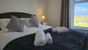A neatly made bed with pillows, a bedside lamp, and rolled towels. - Large coastal home in the countryside of Amlwch - Pass the Keys (Amlwch)