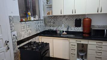 Una cocina con armarios blancos, encimera negra, estufa, fregadero y microondas.