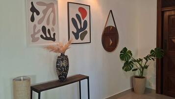 Um corredor com um console de madeira escura, um vaso com plantas secas, arte abstrata na parede, um vaso de planta e um tapete texturizado.