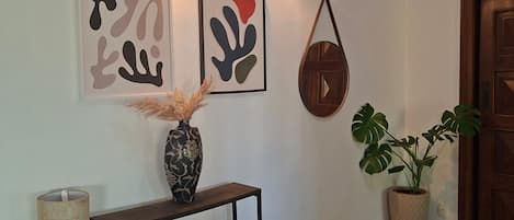 A hallway with a dark wooden console table, a vase with dried plants, abstract wall art, a potted plant, and a textured rug.
