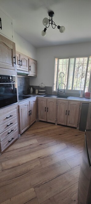 A kitchen with wooden cabinets, a built-in oven, a sink, and a window with a view of trees. - Fully renovated 3-room apartment, quiet and close to downtown (Vence)