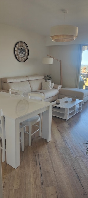 A modern living room with a white sofa, a dining table, and a hanging light fixture. - Fully renovated 3-room apartment, quiet and close to downtown (Vence)