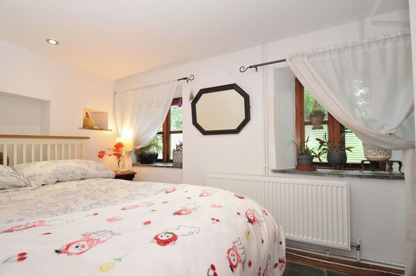 Ein Schlafzimmer mit Bett, einem Fenster mit Vorhängen, einem Heizkörper und einem an der Wand befestigten Spiegel.