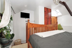 Ein Schlafzimmer mit einem hölzernen Bett, einem an der Wand befestigten Fernseher, einem Kleiderschrank und einem Dachfenster.