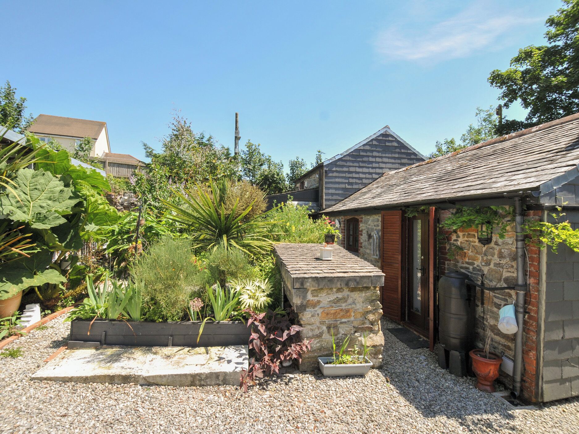 Un jardin agrémenté d’une structure en pierre, d’un abri en bois et d’une maison en arrière-plan.