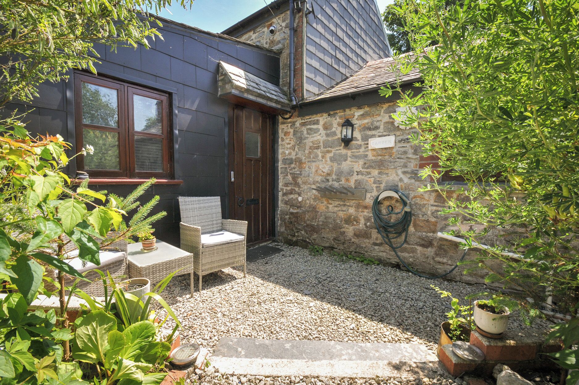 A stone wall with a water spigot, a wicker chair, and a potted plant.