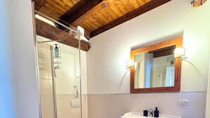 A bathroom with a glass shower enclosure, a white sink with a wooden vanity, and a wooden ceiling. - Biffi Rooms (Bassano del Grappa)