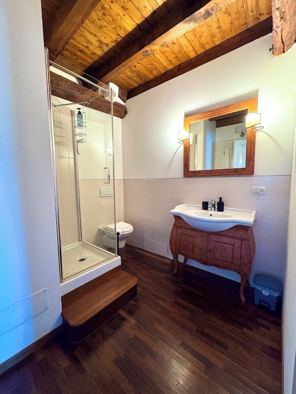 A bathroom with a glass shower enclosure, a white sink with a wooden vanity, and a wooden ceiling.