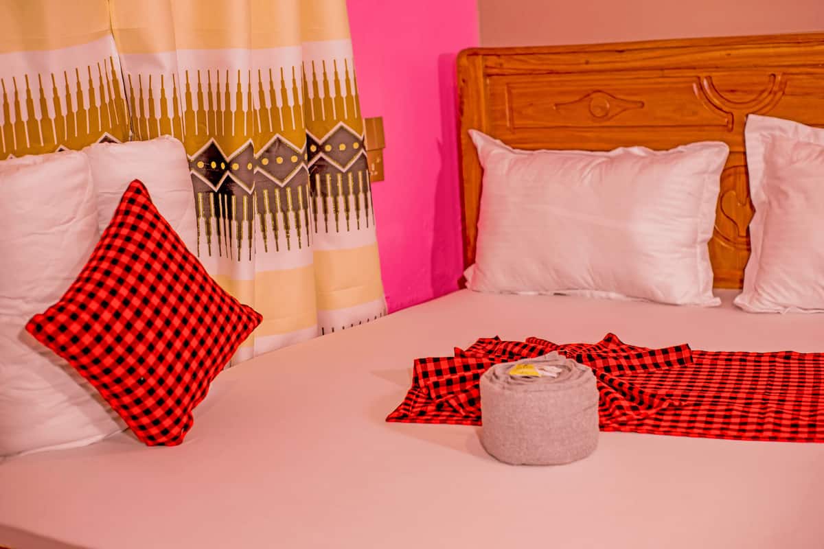 Een bed met witte en rode geruite kussens, een grijze, cilindervormige voorwerp, en een rood-zwarte geruite deken.