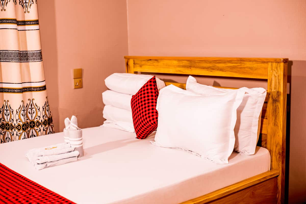 Een net opgemaakt bed met witte lakens, een rood geruit kussen en een houten hoofdbord.
