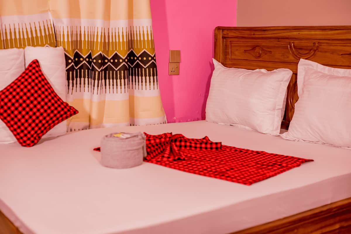 Een bed met wit-rode geruite beddengoed, een grijs kussen en een houten hoofdbord.