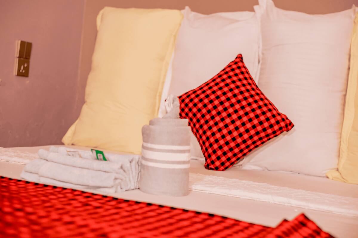 Een bed met witte en rode geruite kussens, een wit kussen en een fles water.