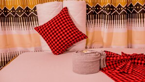 Una cama con un cojín rojo y negro a cuadros, un cojín gris y una manta a rayas.