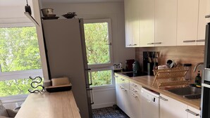 Eine moderne Küche mit einem Holztisch, weißen Schränken, einem gemusterten Boden und einem Fenster mit Blick auf Bäume.