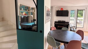 Eine moderne Küche mit einer türkisfarbenen Akzentwand, ein Essbereich mit rundem Tisch und Stühlen sowie eine Treppe, die eine weitere Ebene hinaufführt.