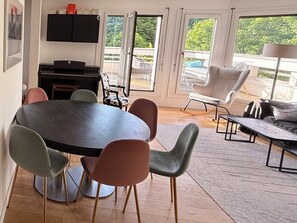 Ein modernes Wohnzimmer mit einem runden Tisch, mehreren Stühlen, einem Sofa, einem Couchtisch und einem Fernseher.